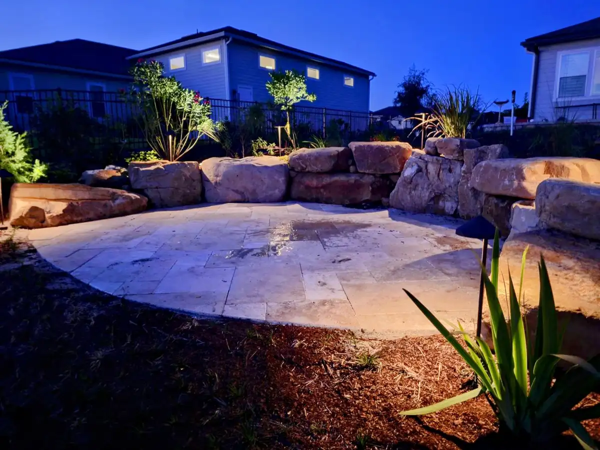 Landscape lights illuminating a stone patio, boulders and small trees at night